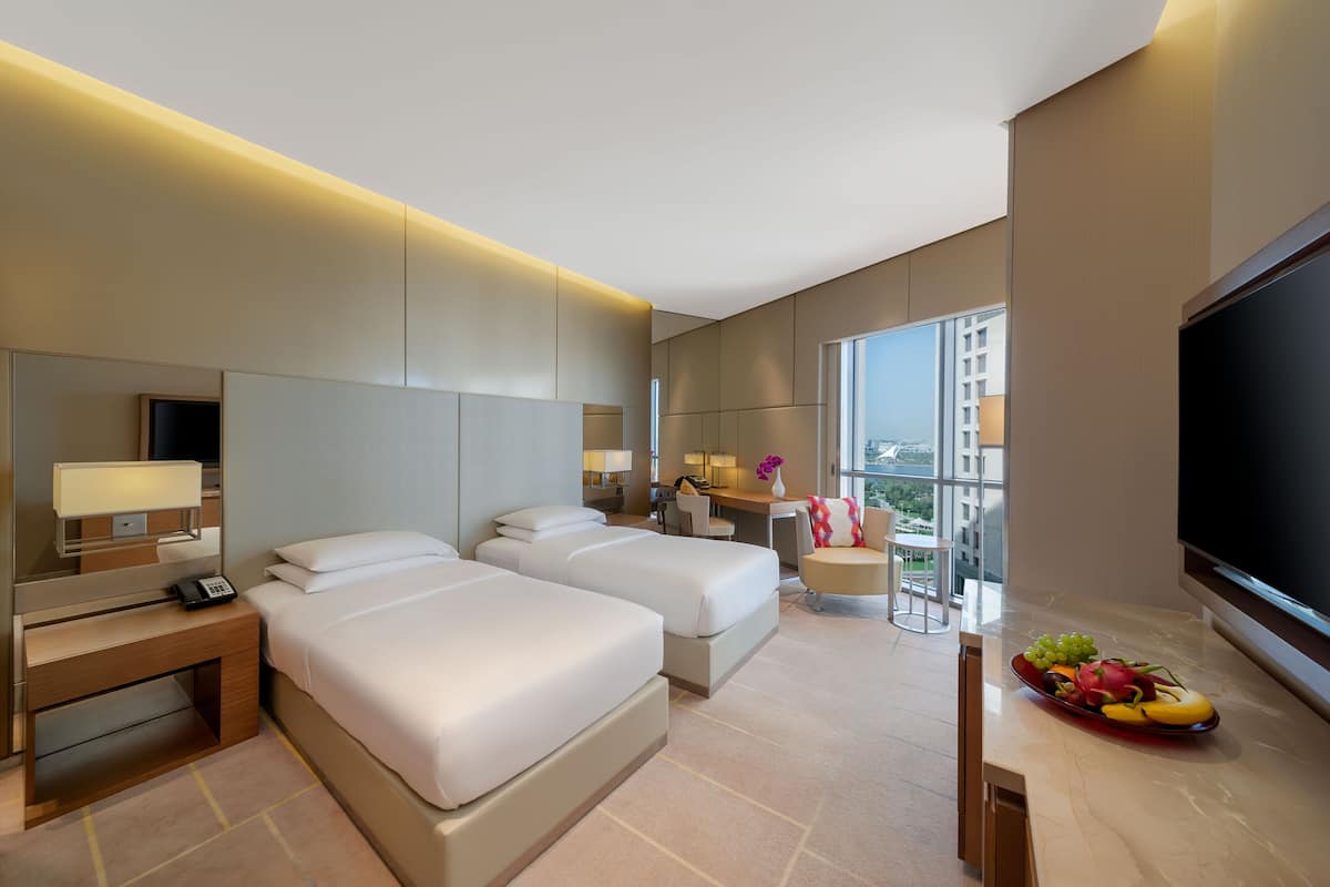 Ein modernes Hotelzimmer mit zwei Betten, einem Schreibtisch, einem Fernseher und einem Balkon mit Blick.