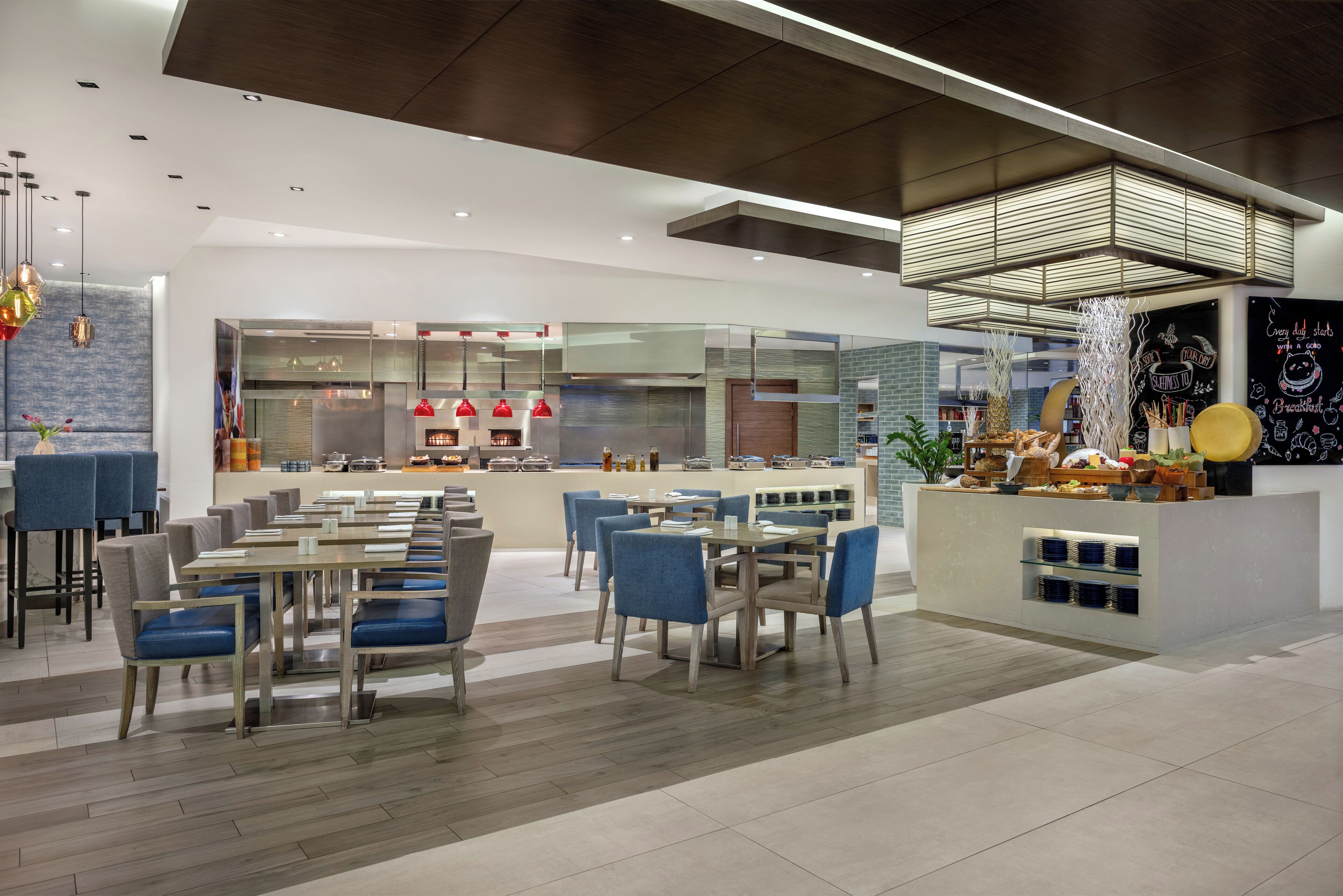 Un ristorante moderno con un'area bar centrale, diverse opzioni di posti a sedere e una cucina a vista sullo sfondo.