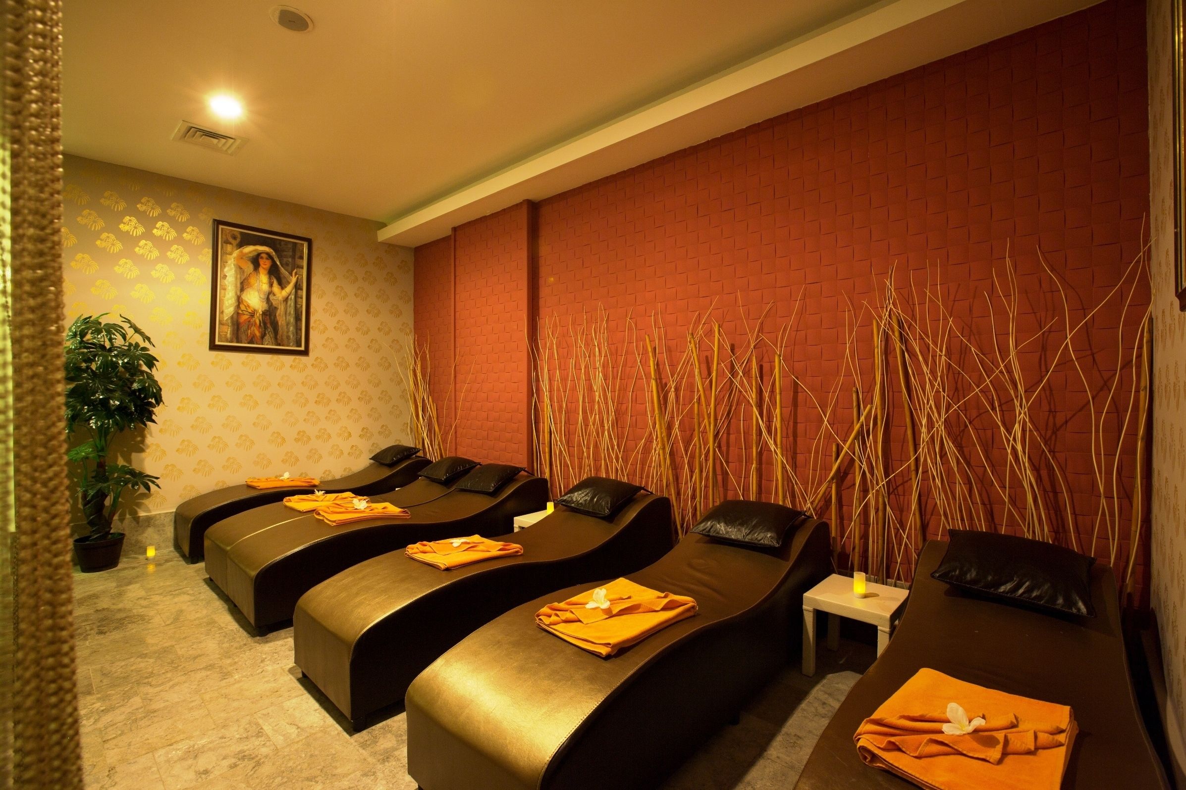 A spa room with two massage tables, a small table with a candle, and a potted plant.