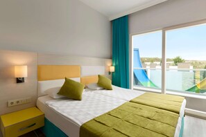 A hotel room with a bed, a nightstand, a window with a view of a slide and buildings, and a teal curtain. - Ramada Resort by Wyndham Side (Manavgat)