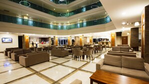 Um hall de hotel em vários níveis, com área de estar central, diversos andares e guarda-corpo de vidro.