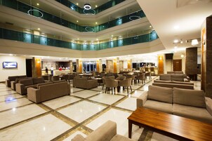 Um hall de hotel em vários níveis, com área de estar central, diversos andares e guarda-corpo de vidro.