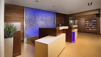 Zona de recepción con un mostrador de madera, una pared azul iluminada y una pequeña tienda con aperitivos.