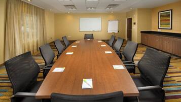 A conference room with a long wooden table, black chairs, a whiteboard, and a projector screen.