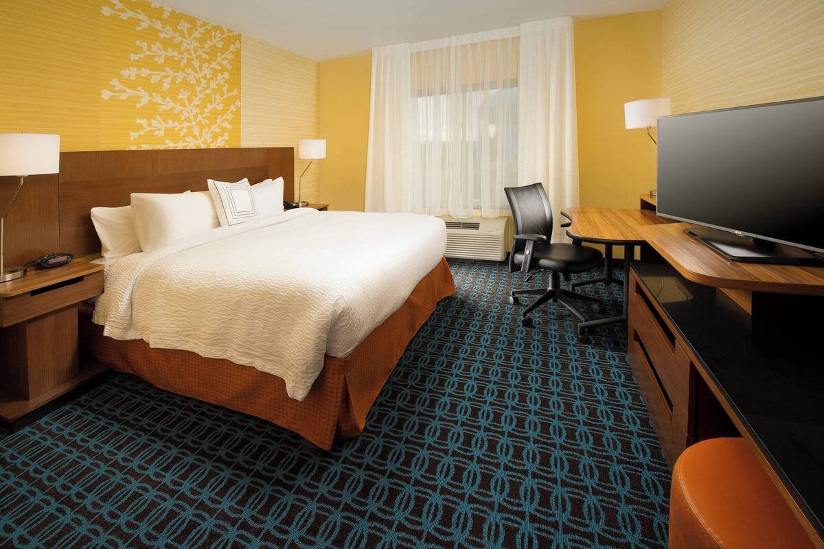 Una habitación de hotel con una cama grande, un escritorio con televisión, una silla y una lámpara de escritorio.
