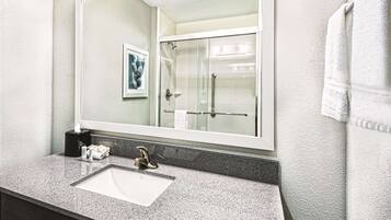 A bathroom with a large mirror, a sink, and a shower.