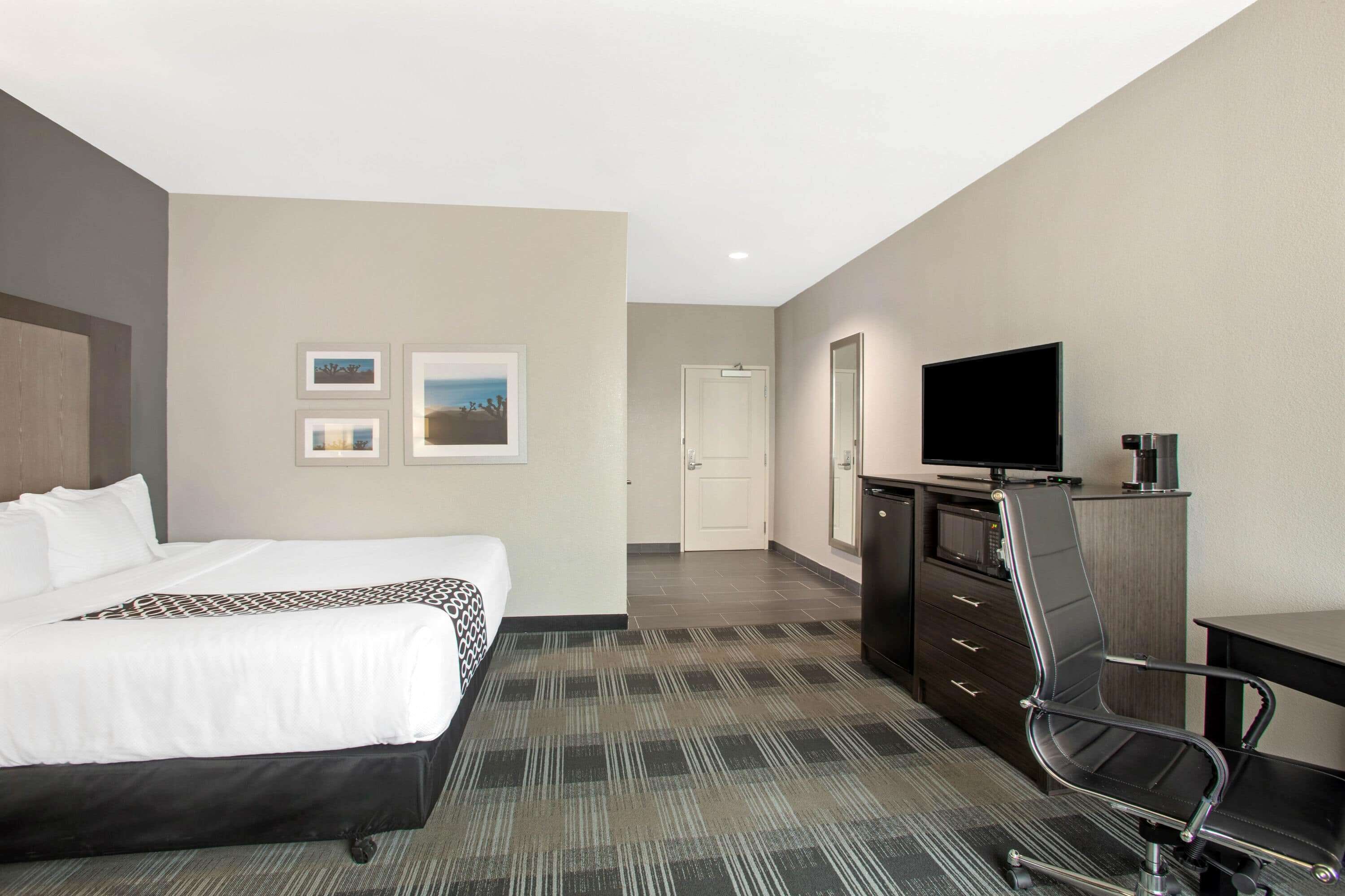 A hotel room with a bed, a desk, a chair, a television, and a door.