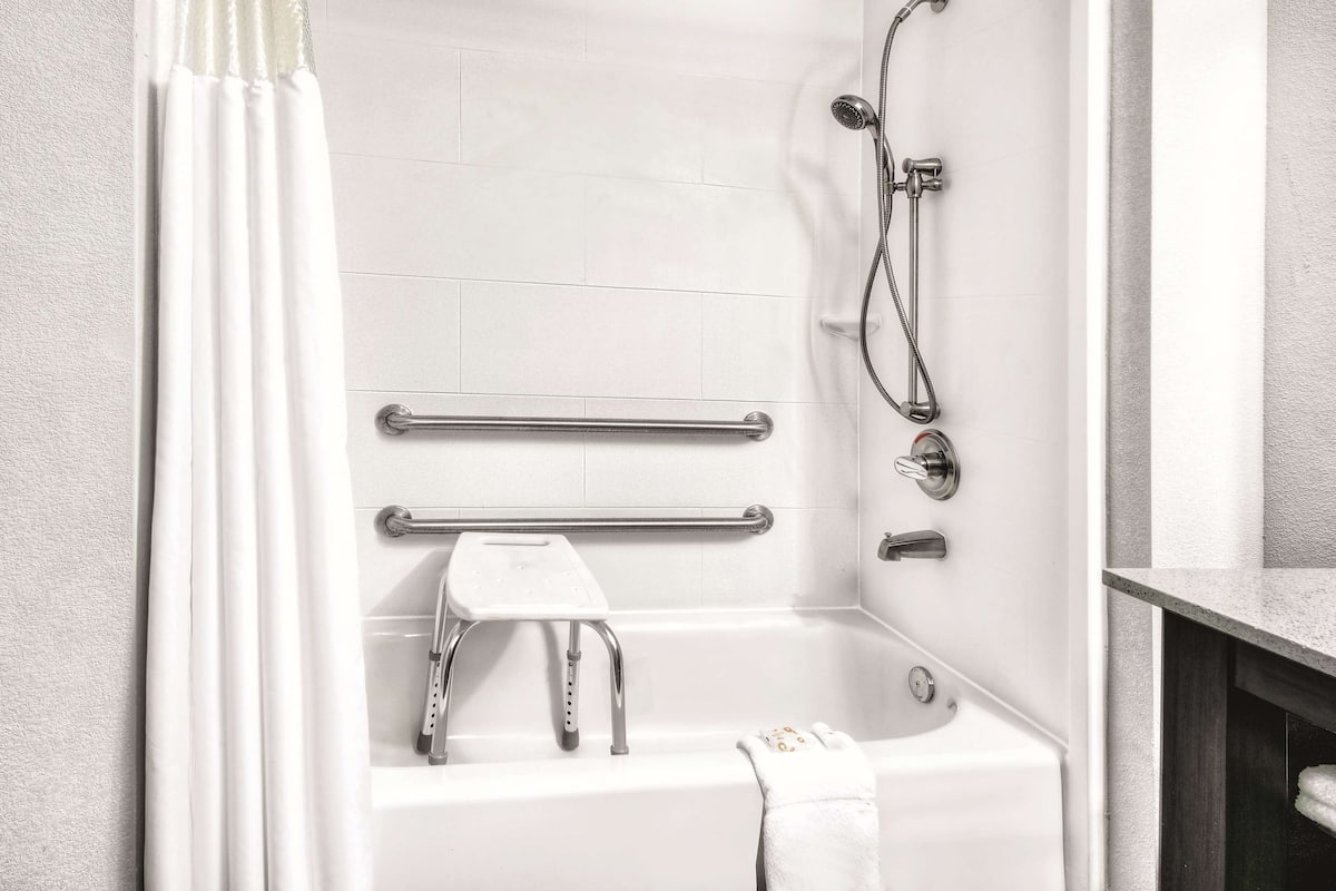 Une salle de bain moderne équipée d’une baignoire, de barres d’appui, d’un pommeau de douche et d’un porte-serviettes.