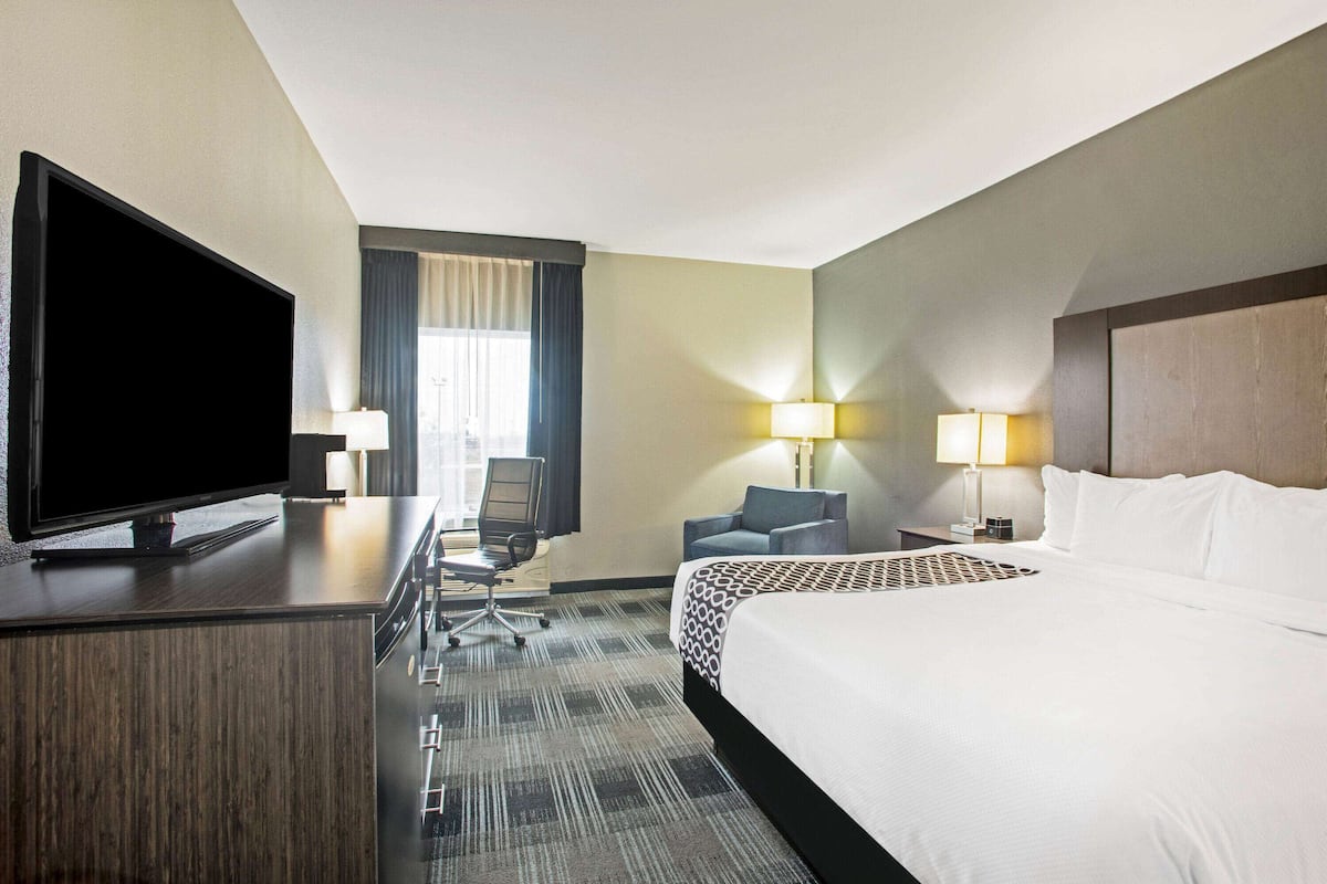 Une chambre d’hôtel dotée d’un grand lit, d’un téléviseur à écran plat, d’un bureau avec une chaise, de deux lampes de chevet et d’une fenêtre avec des rideaux.