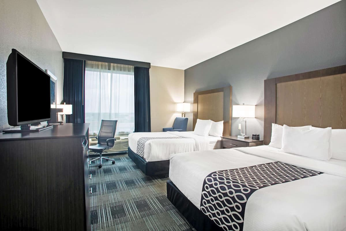 Une chambre d’hôtel avec deux lits, un bureau doté d’un téléviseur à écran plat, une chaise, une lampe de bureau et une vue sur la ville.
