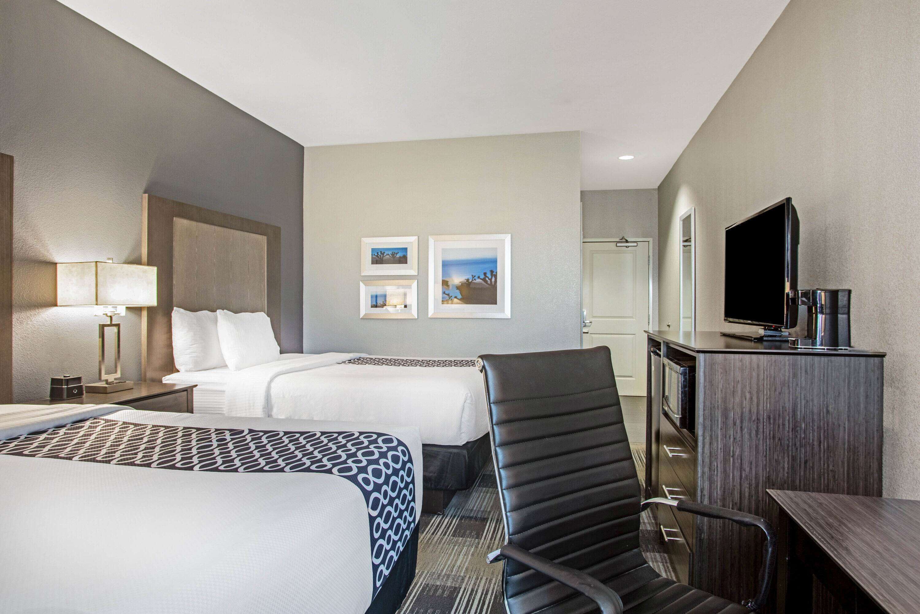 A hotel room with two beds, a desk, a chair, a television, and framed pictures on the wall.