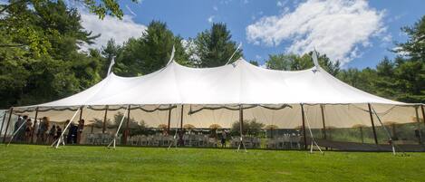 A large white tent set up on a grassy field with tables and chairs underneath.