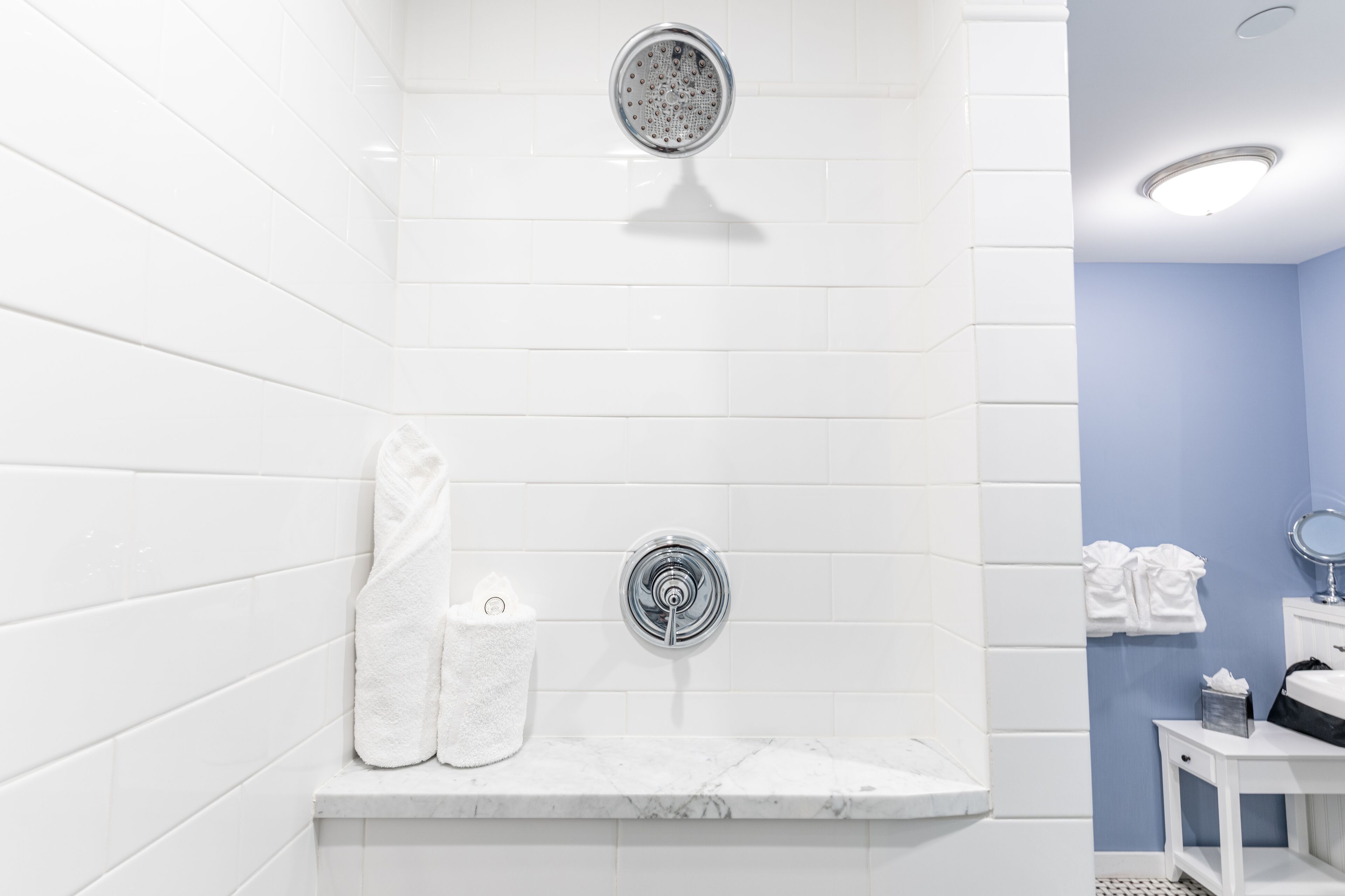 A bathroom with white tiled walls, a marble sink, and a shower with a chrome showerhead.