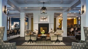 A spacious living room with a fireplace, two armchairs, a coffee table, and a dining area with chairs and a table. - Inn at Diamond Cove (Portland)