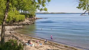 A beach with a wooden staircase leading down to the shore, surrounded by trees and a calm body of water. - Inn at Diamond Cove (Portland)