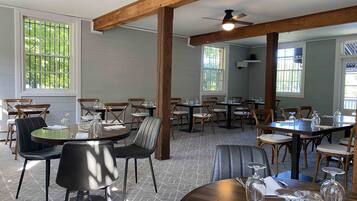 A restaurant with wooden beams, large windows, and a variety of seating arrangements including round tables and chairs.