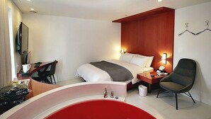 A modern hotel room with a bed, bedside table, chair, desk, and a red bathtub. - Circle Hotel Seoul (Seoul)
