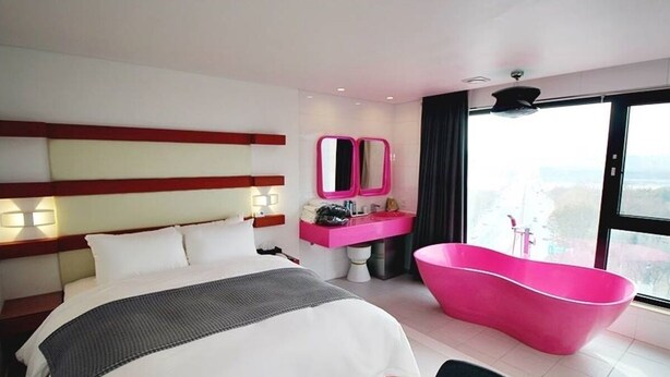 A modern hotel room with a large bed, a pink bathtub, and a city view. - Circle Hotel Seoul (Seoul)