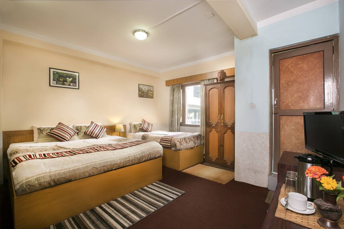 A hotel room with two beds, a television, a coffee maker, and a small table with a cup and flowers.