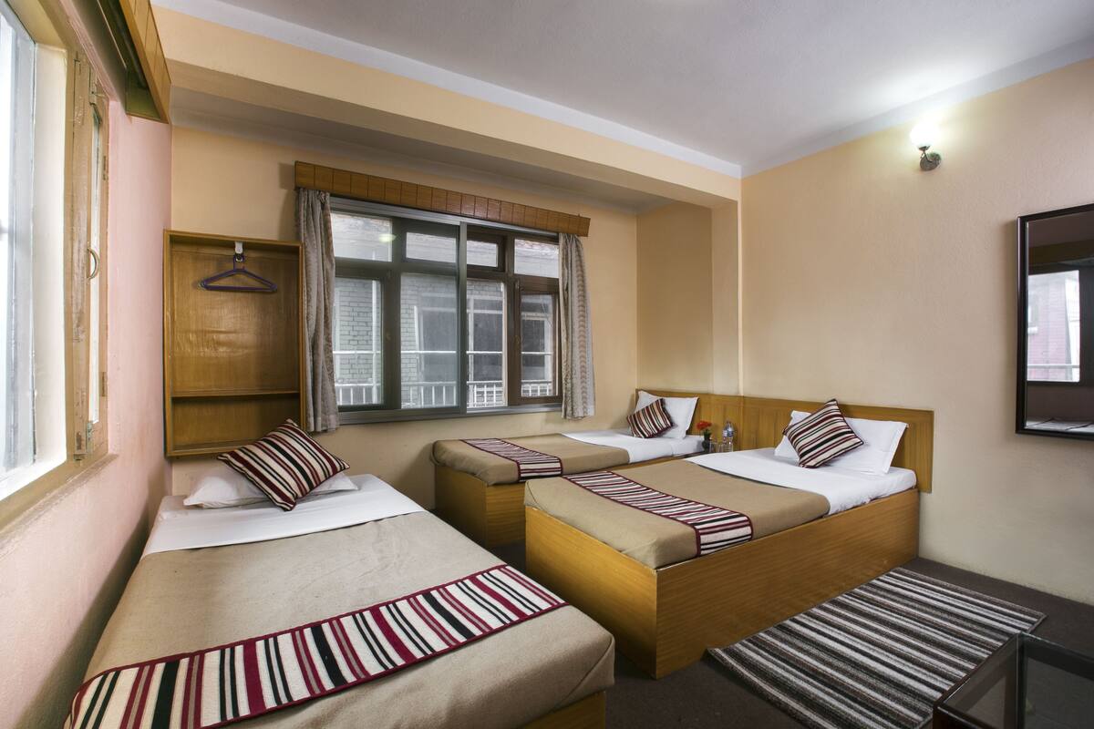 A hotel room with two single beds, a wooden headboard, a window with curtains, and a small table.