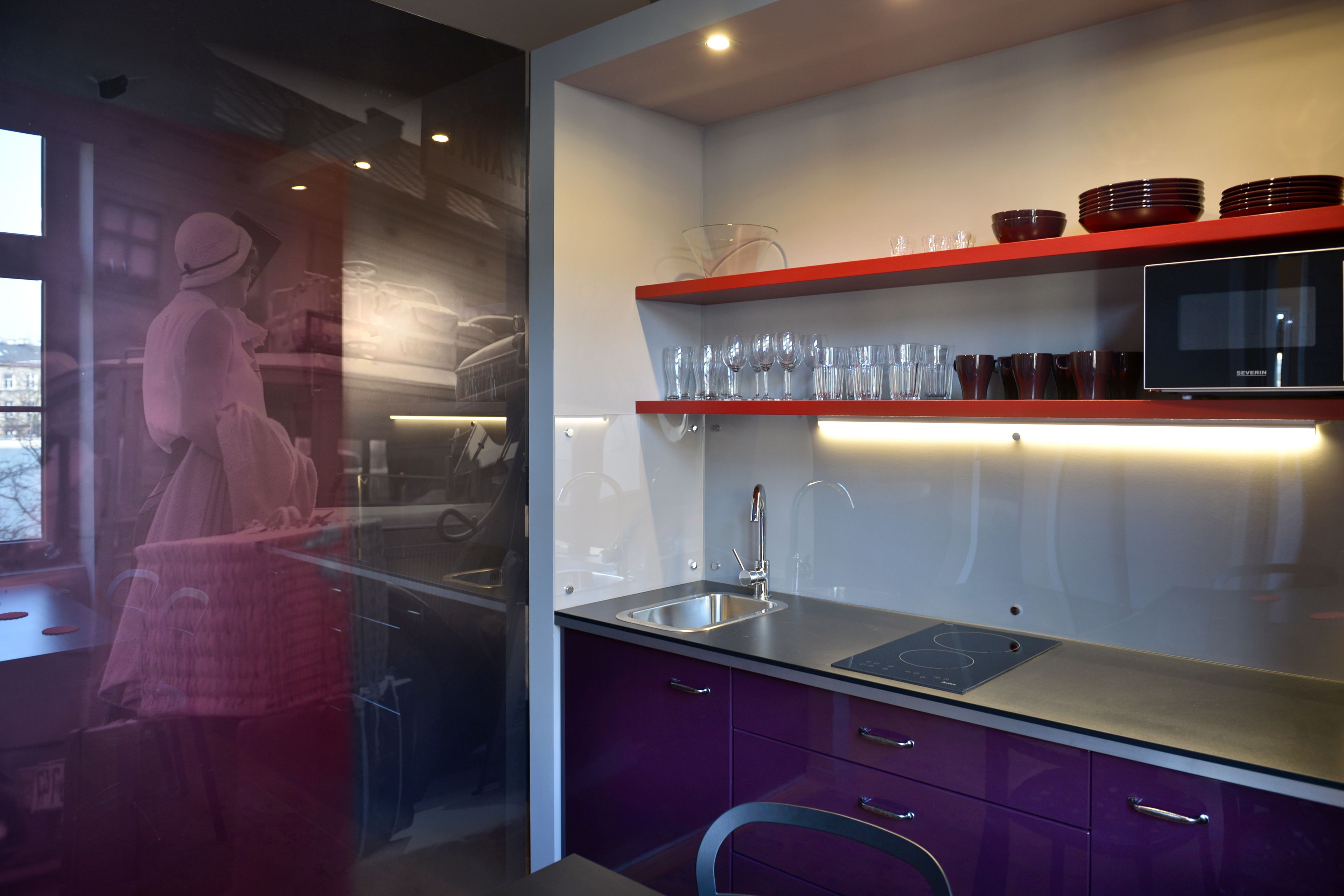 A modern kitchen with a built-in microwave, a stainless steel sink, and red shelves holding glassware.