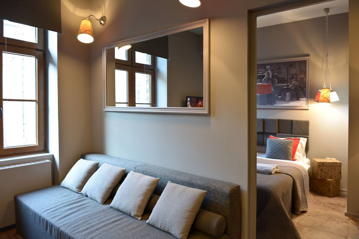 Quarto moderno com sofá cinza, um espelho grande e uma cama com cabeceira.