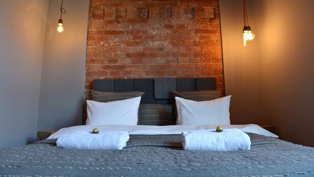 A bed with white linens, a brick wall behind it, and two hanging light bulbs.