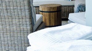 Een woonkamer met een rieten stoel, een ronde houten tafel en een bank met gekleurde kussens.