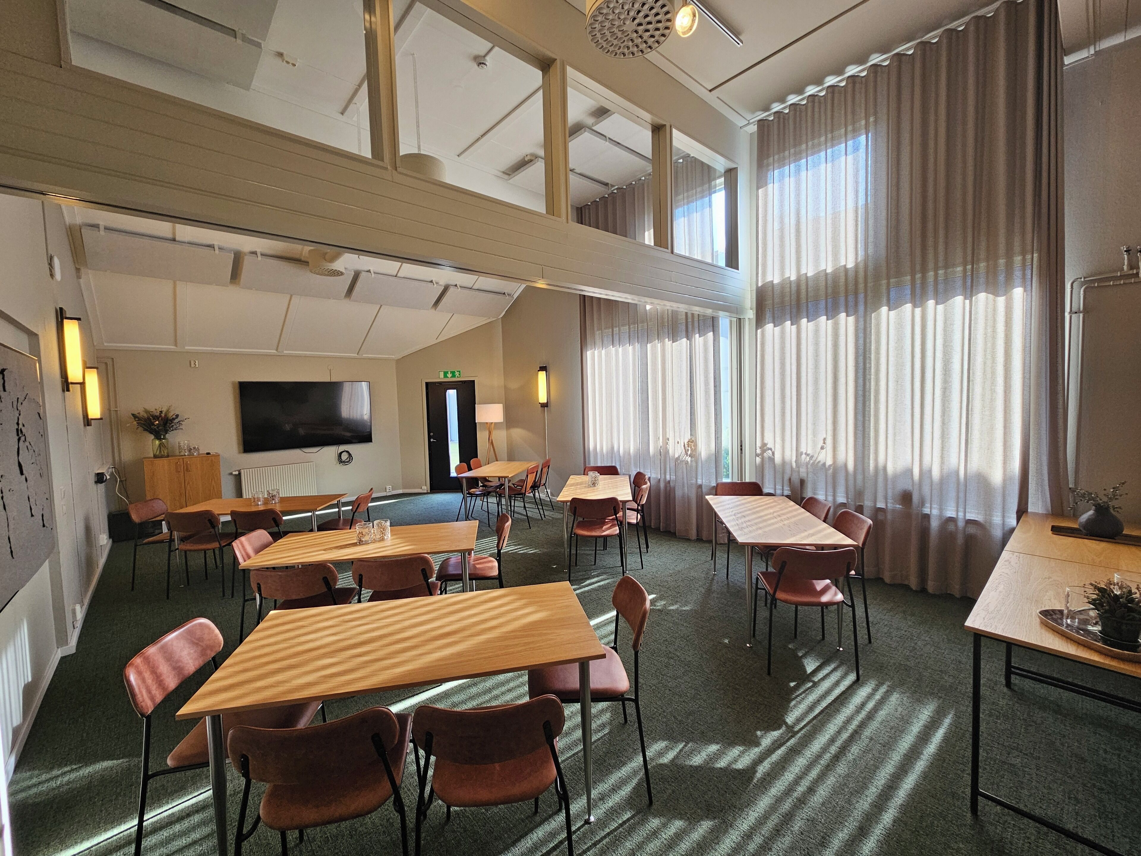 A hotel room with a large bed, a TV, and a desk with chairs. There is a window with curtains and a view of the outside.