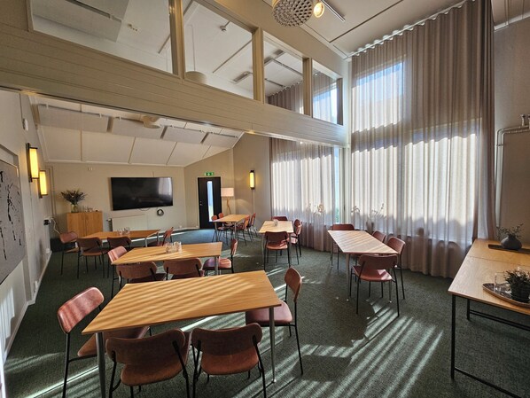 Habitación de hotel con una cama grande, televisión y escritorio con sillas. Tiene ventana con cortinas y vistas al exterior.