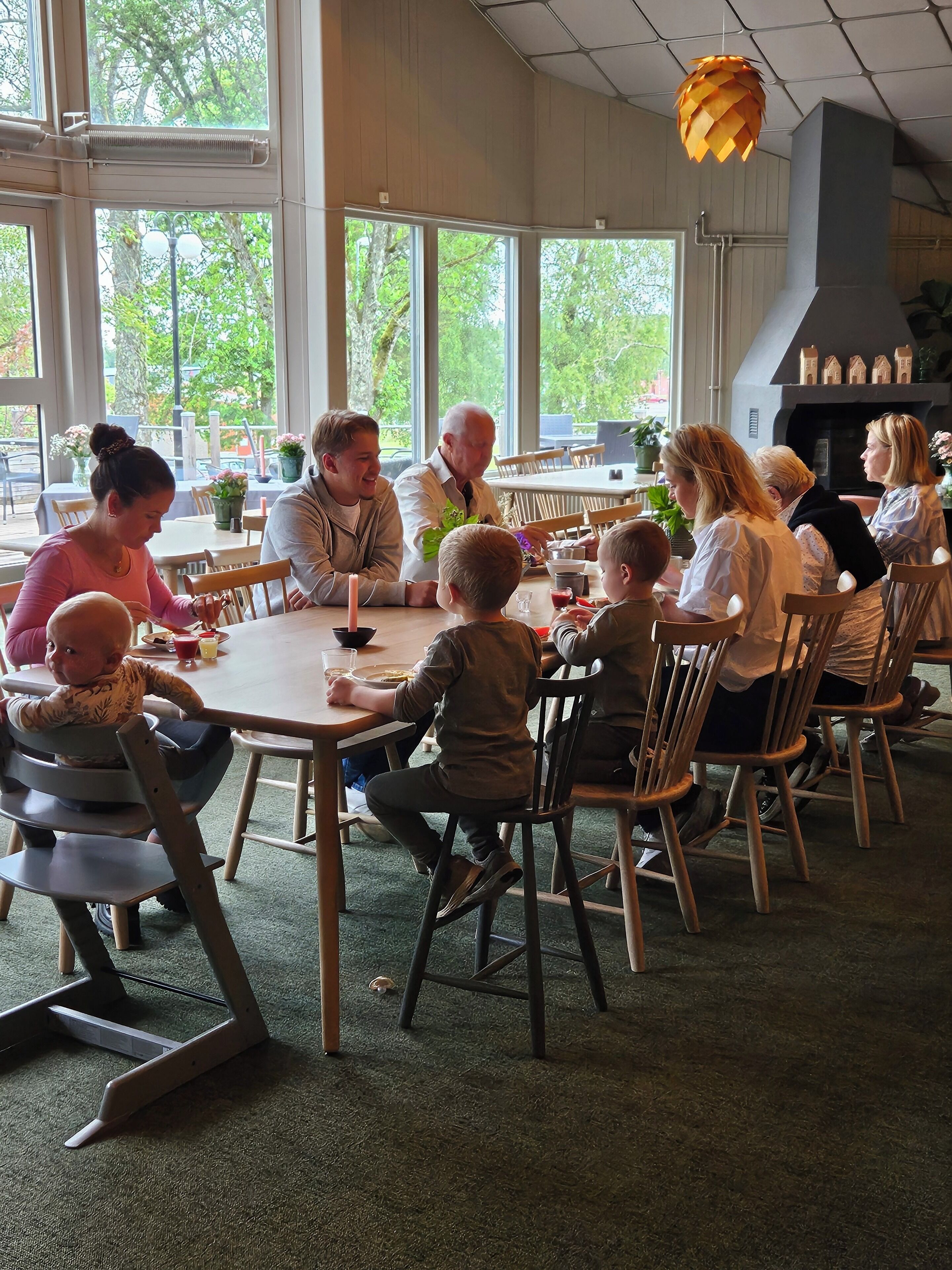 A family dining at a restaurant with large windows, a fireplace, and a ceiling light fixture.