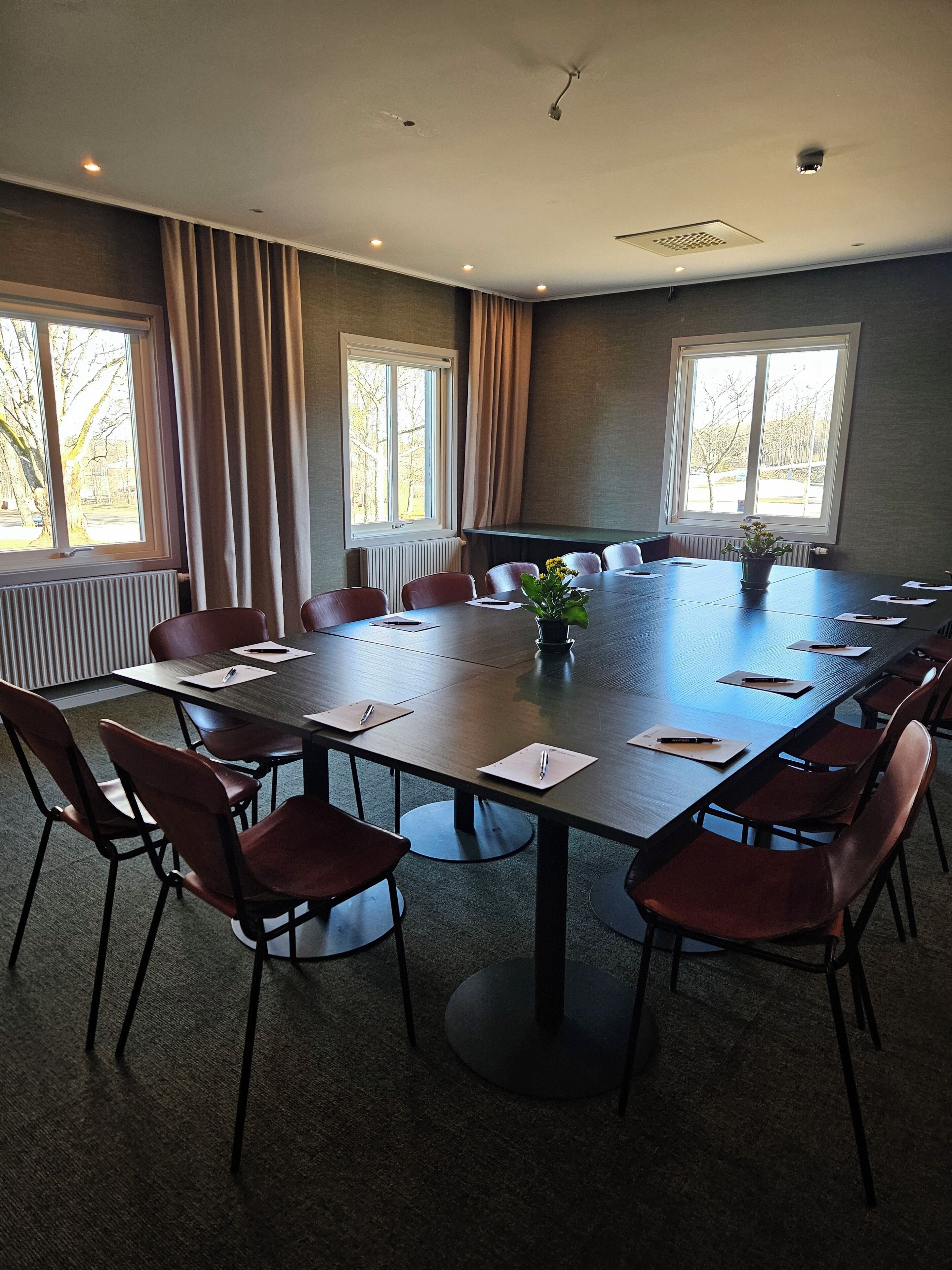 Un salón de conferencias con una gran mesa, sillas y ventanas con cortinas.