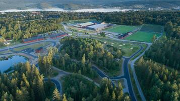 Vue aérienne d’un complexe sportif comprenant plusieurs terrains, des bâtiments et un lac en arrière-plan.