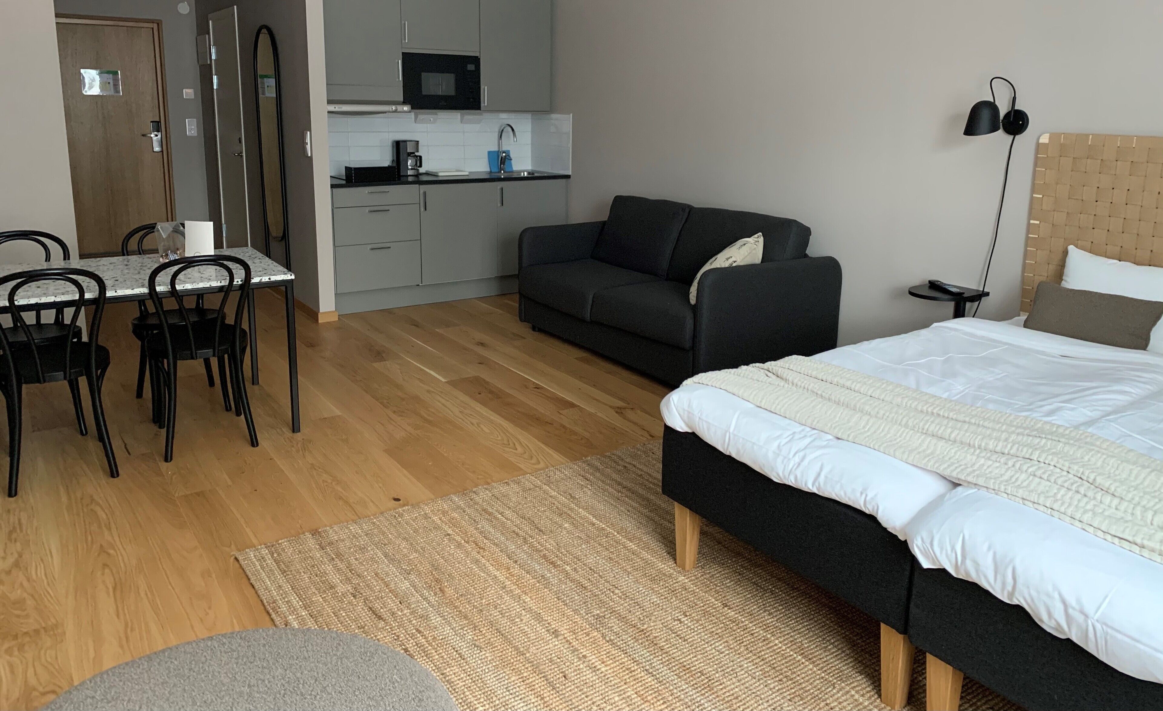 Un dormitorio compacto con cama, sofá, mesa de comedor con sillas, zona de cocina y una pequeña mesita.