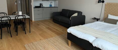 Un dormitorio compacto con cama, sofá, mesa de comedor con sillas, zona de cocina y una pequeña mesita.