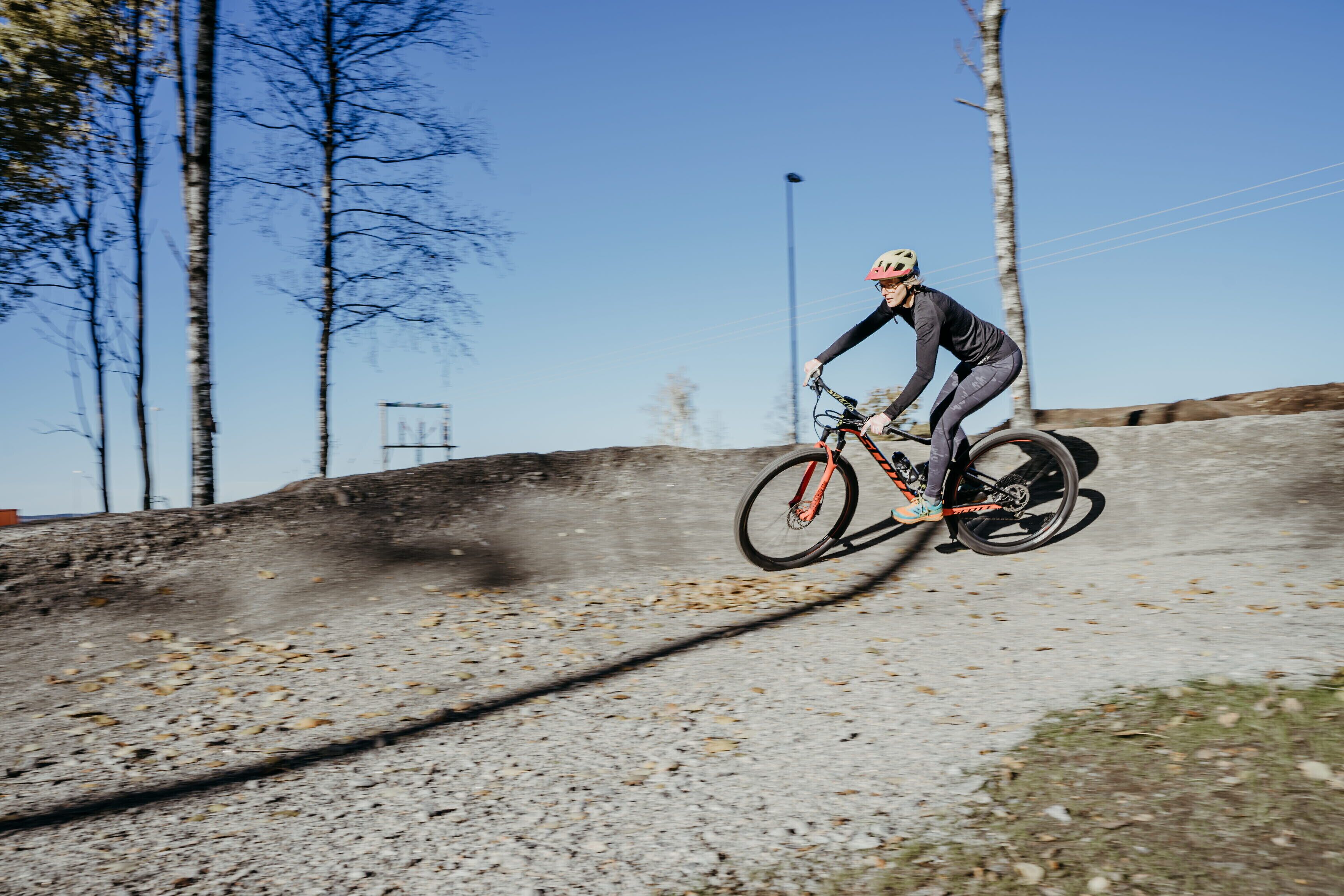 A person riding a bicycle on a dirt path with trees and a clear sky in the background.