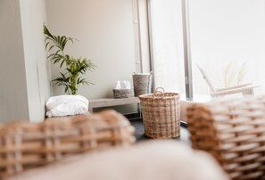 Una habitación con un ventanal grande, una planta, cestas de mimbre y una cama bien hecha.