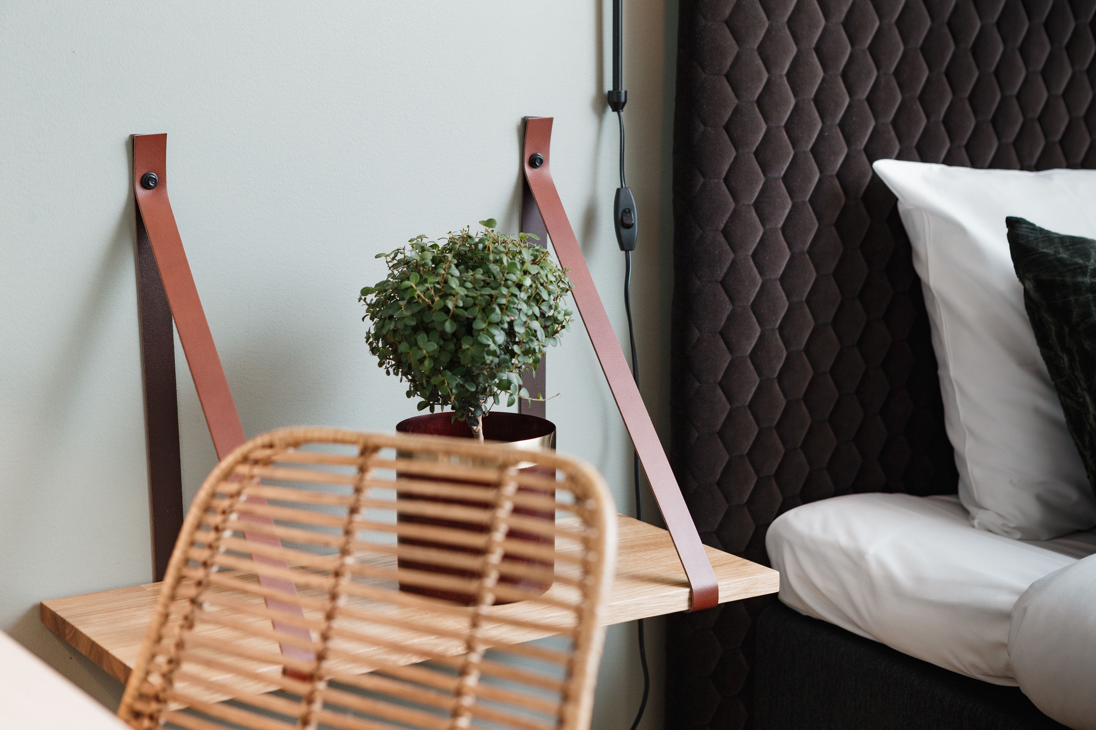 A modern room with a wooden chair, a small potted plant, and a bed with white bedding.