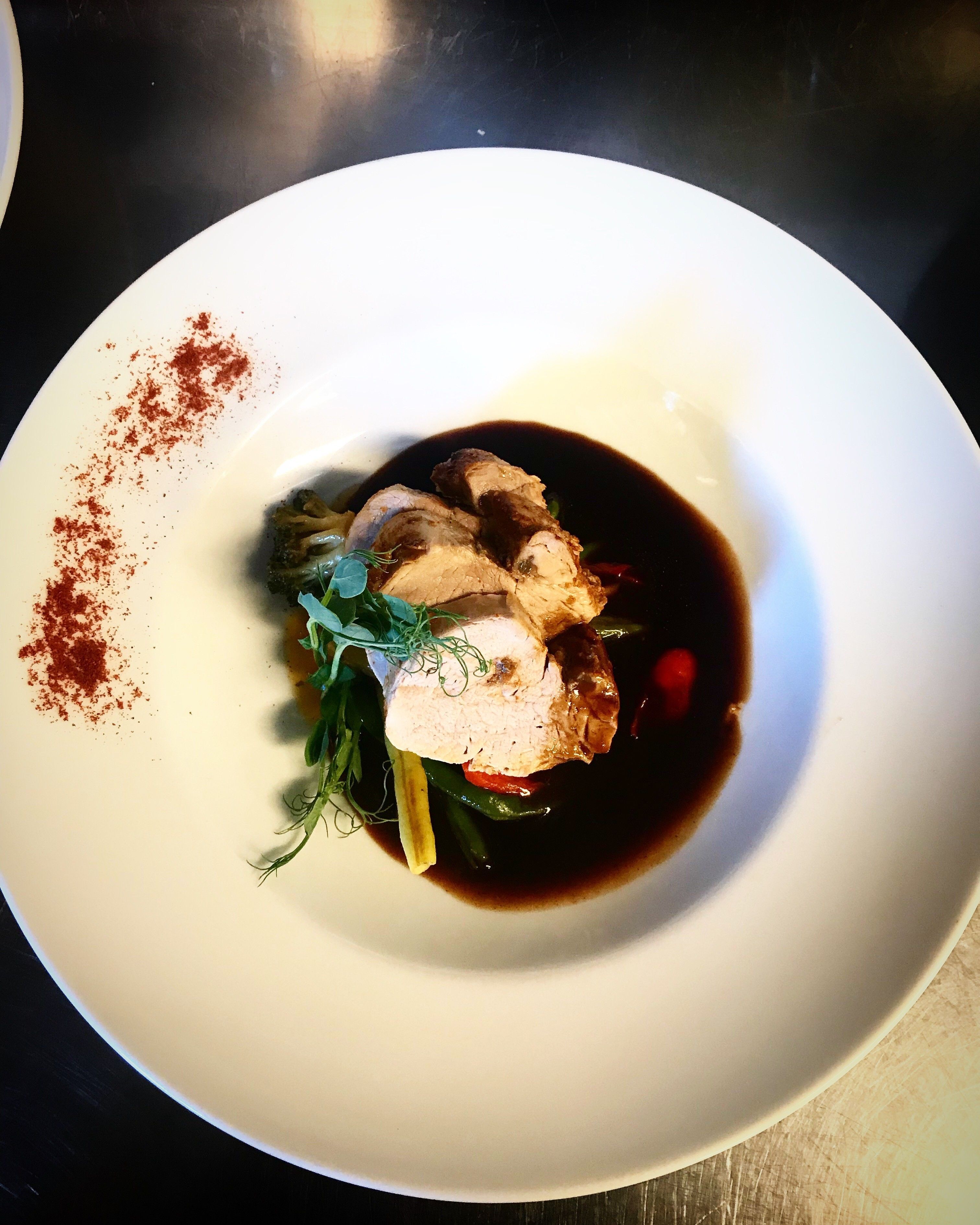A white plate with a dish consisting of meat, vegetables, and a dark sauce.