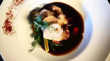 A white plate with a dish consisting of meat, vegetables, and a dark sauce.