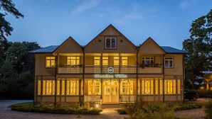 Een houten villa met twee verdiepingen, een balkon, een bord met de tekst 'Wooden Villa' en een goed verlichte entree.