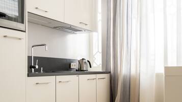 A modern kitchen with white cabinets, a black countertop, and a kettle.