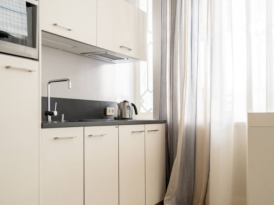 A modern kitchen with white cabinets, a black countertop, and a kettle.