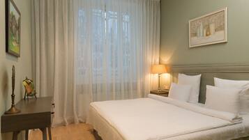 Een hotelkamer met een bed, een nachtkastje met een lamp, een tafeltje met een fotolijstje en een raam met dunne gordijnen.