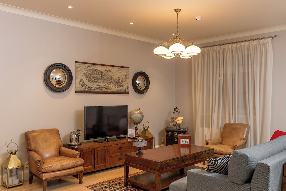Un salon comprenant une télévision, des fauteuils en cuir, un canapé, une table basse en bois, un globe terrestre et un lustre.