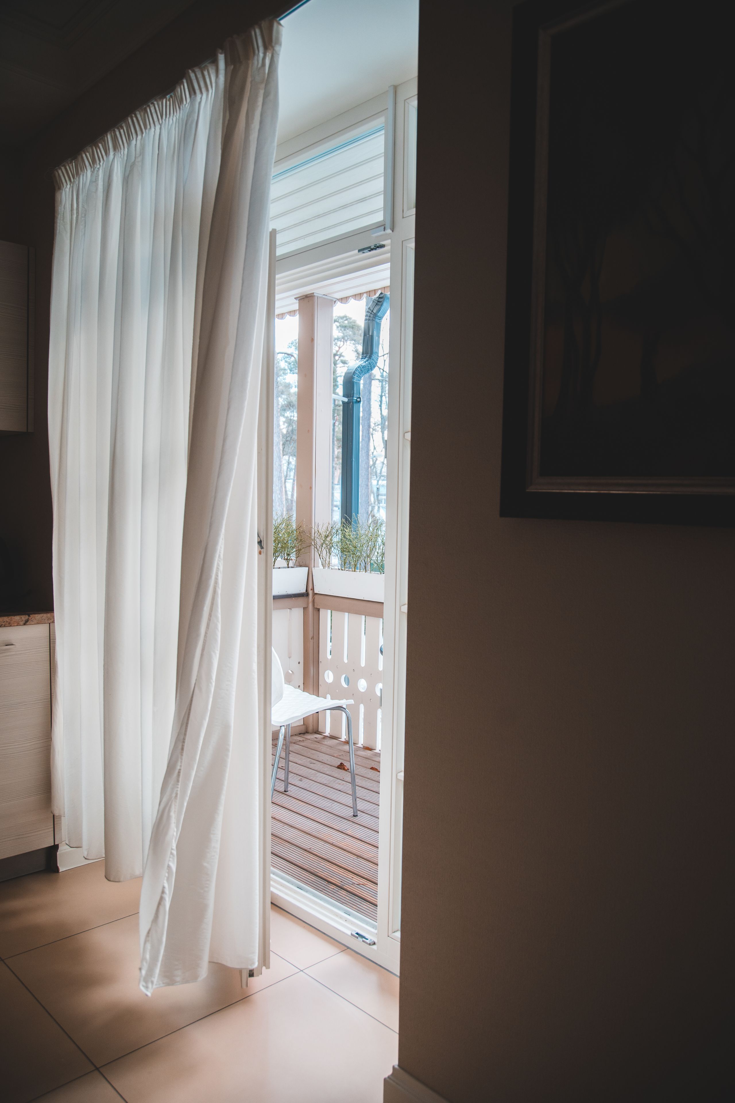 Una habitación con cortina blanca, una silla blanca y vistas a un balcón con barandilla.