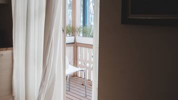 Una habitación con cortina blanca, una silla blanca y vistas a un balcón con barandilla.