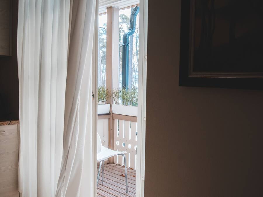 Una habitación con cortina blanca, una silla blanca y vistas a un balcón con barandilla.