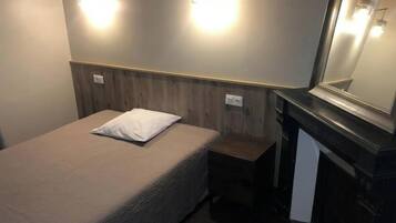 Habitación de hotel con cama, mesita de noche, espejo e iluminación en la pared.