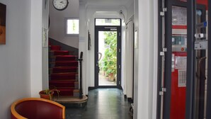 A hallway with a staircase, a clock, and a door leading to an outdoor area with plants. - Hotel Residence Champerret (Levallois-Perret)